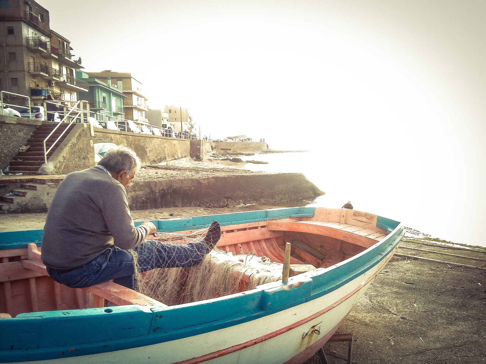 93910675 Side view of fisherman repairing fishing net while sitting on rowboat